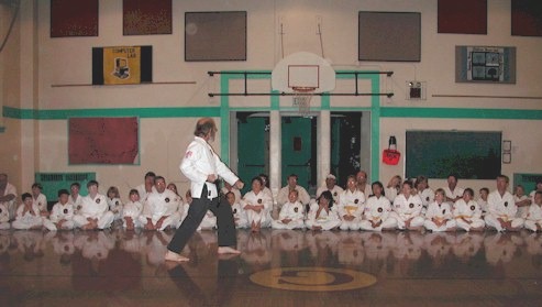 A person in white uniform standing in front of a group of people

Description automatically generated